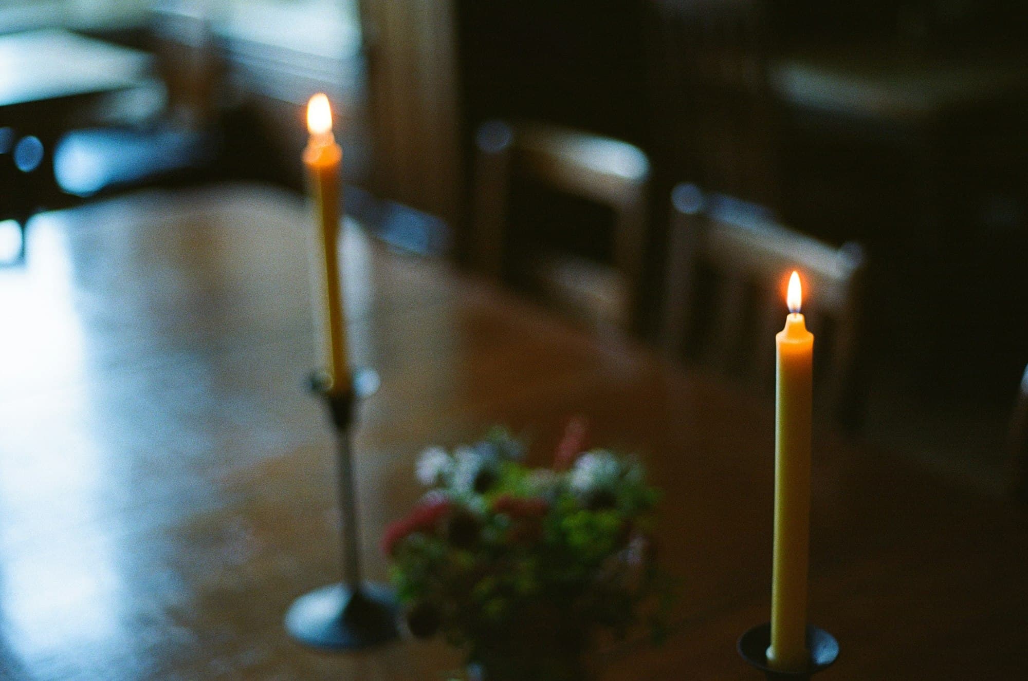 Two beeswax taper candles lit on a wooden table in soft warm light
